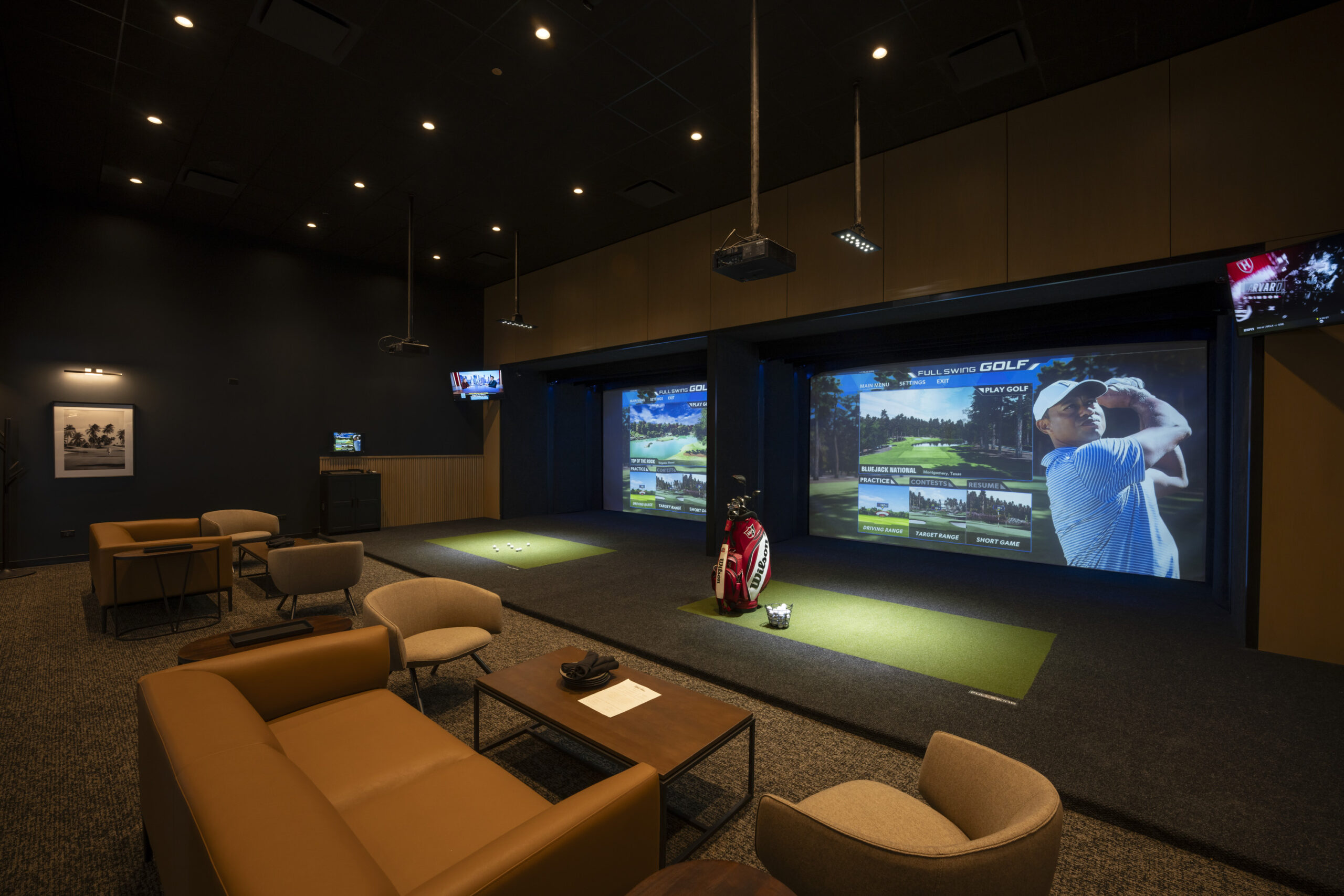 Two modern golf simulators featuring large projection screens, stage lighting and lounge seating.