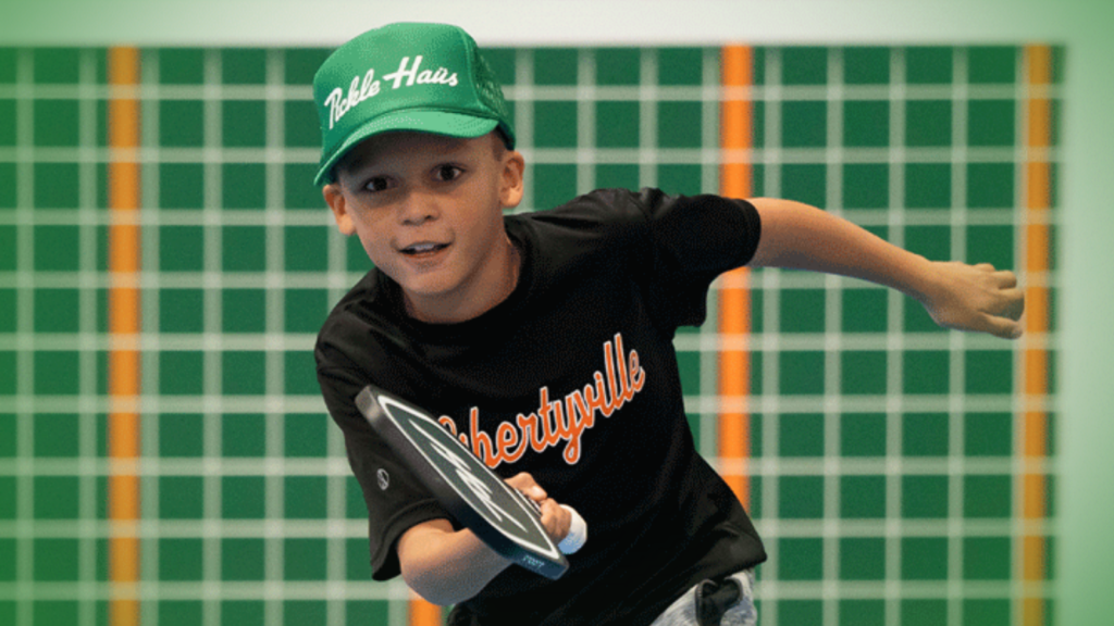 Young boy wearing green Pickle Haus hat playing pickleball with winter snowflake border around image.