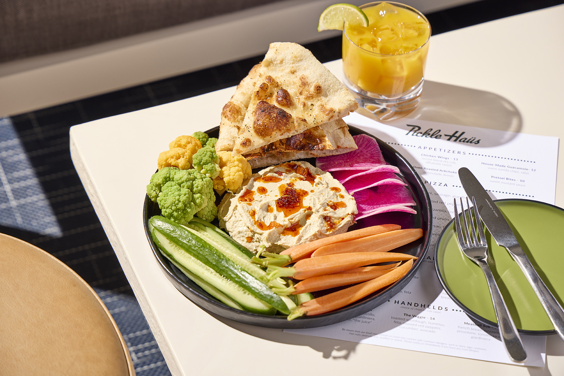 hummus platter with bread and vegetables on table with mixed drink and menu