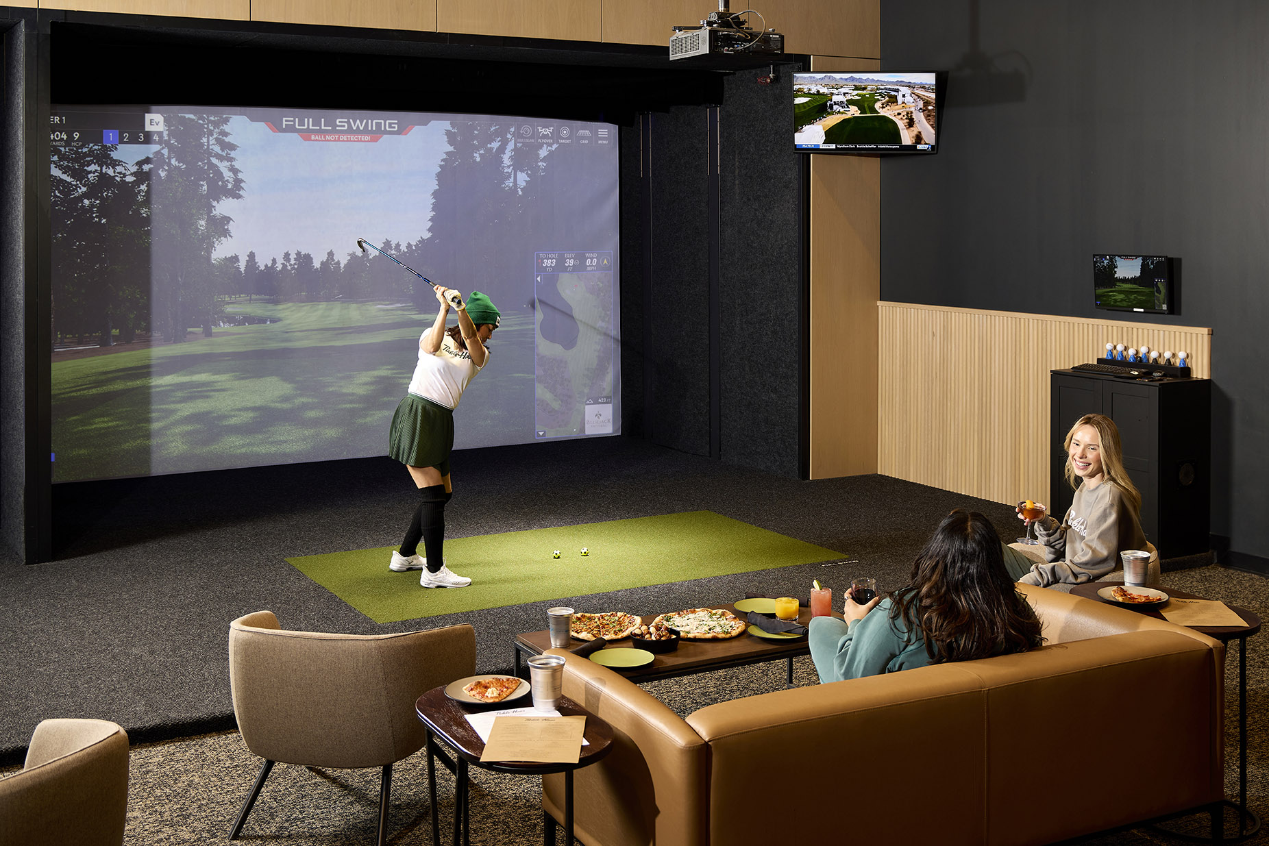 woman playing on golf simulator with friends talking