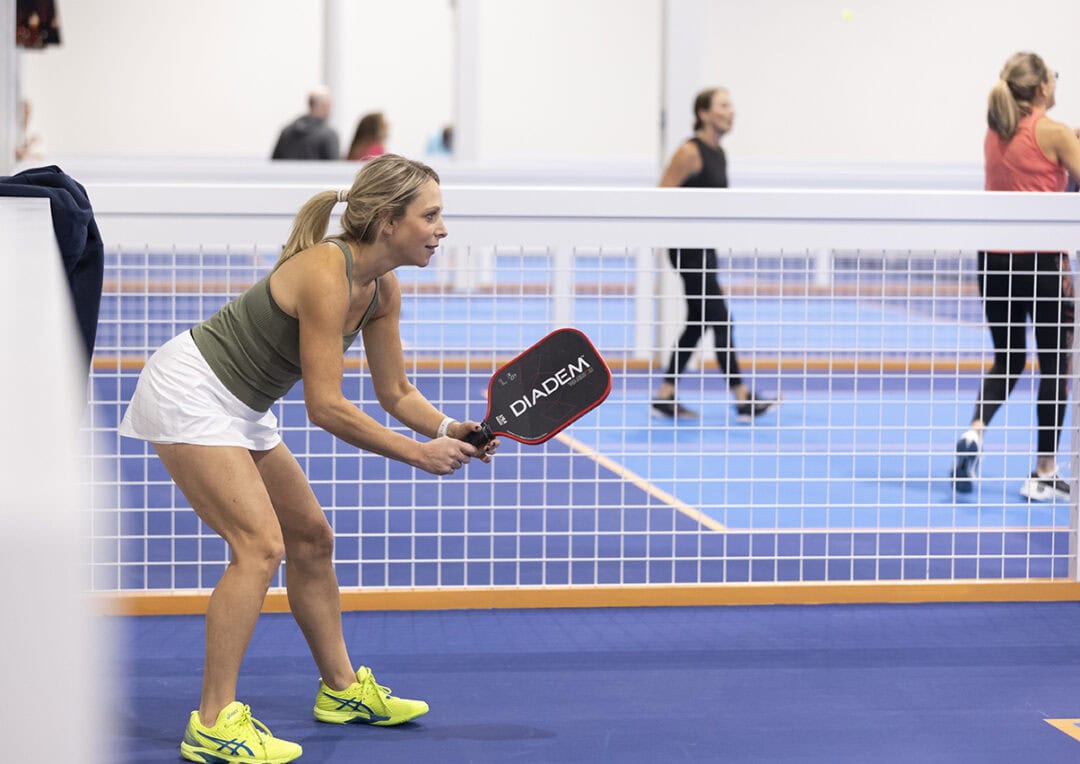 Woman holding a pickleball paddle and preparing for a serve on the court