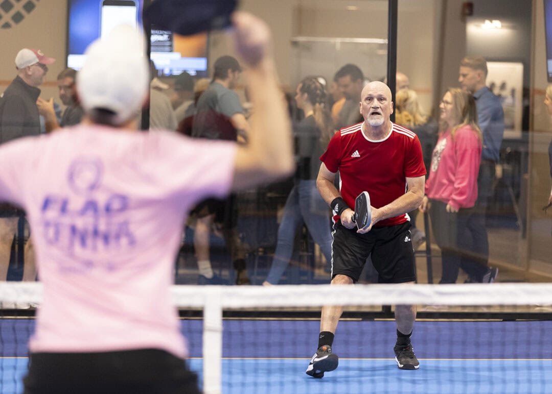 Two men competing in a pickleball game, one in focus holding the paddle, while the other is blurred in the background